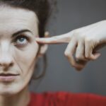 selective focus portrait photo of woman in red t shirt pointing to her head
